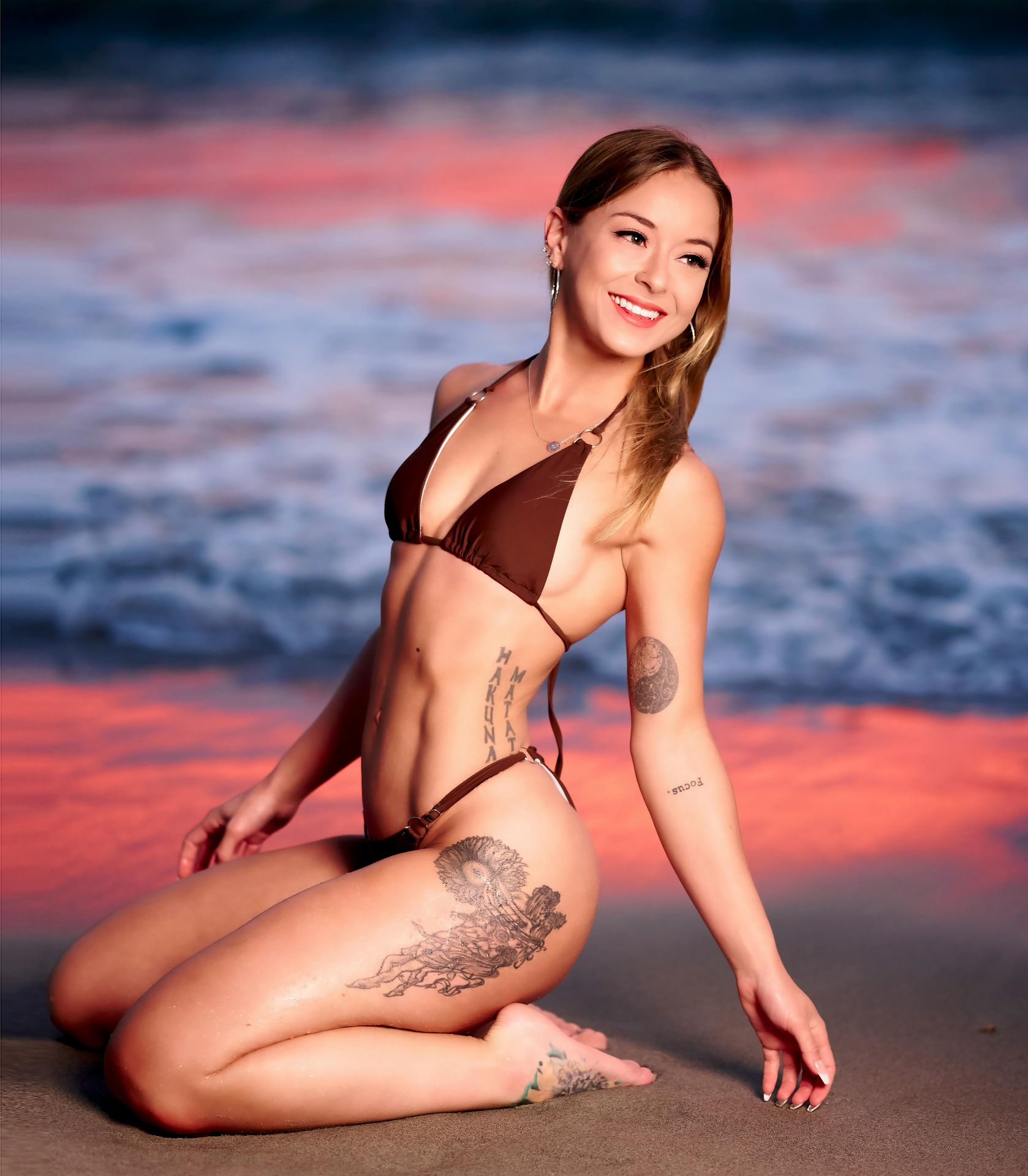 A confident woman posing on the beach at sunset, gazing at the ocean with a radiant glow, embodying empowerment and self-love in her bikini.