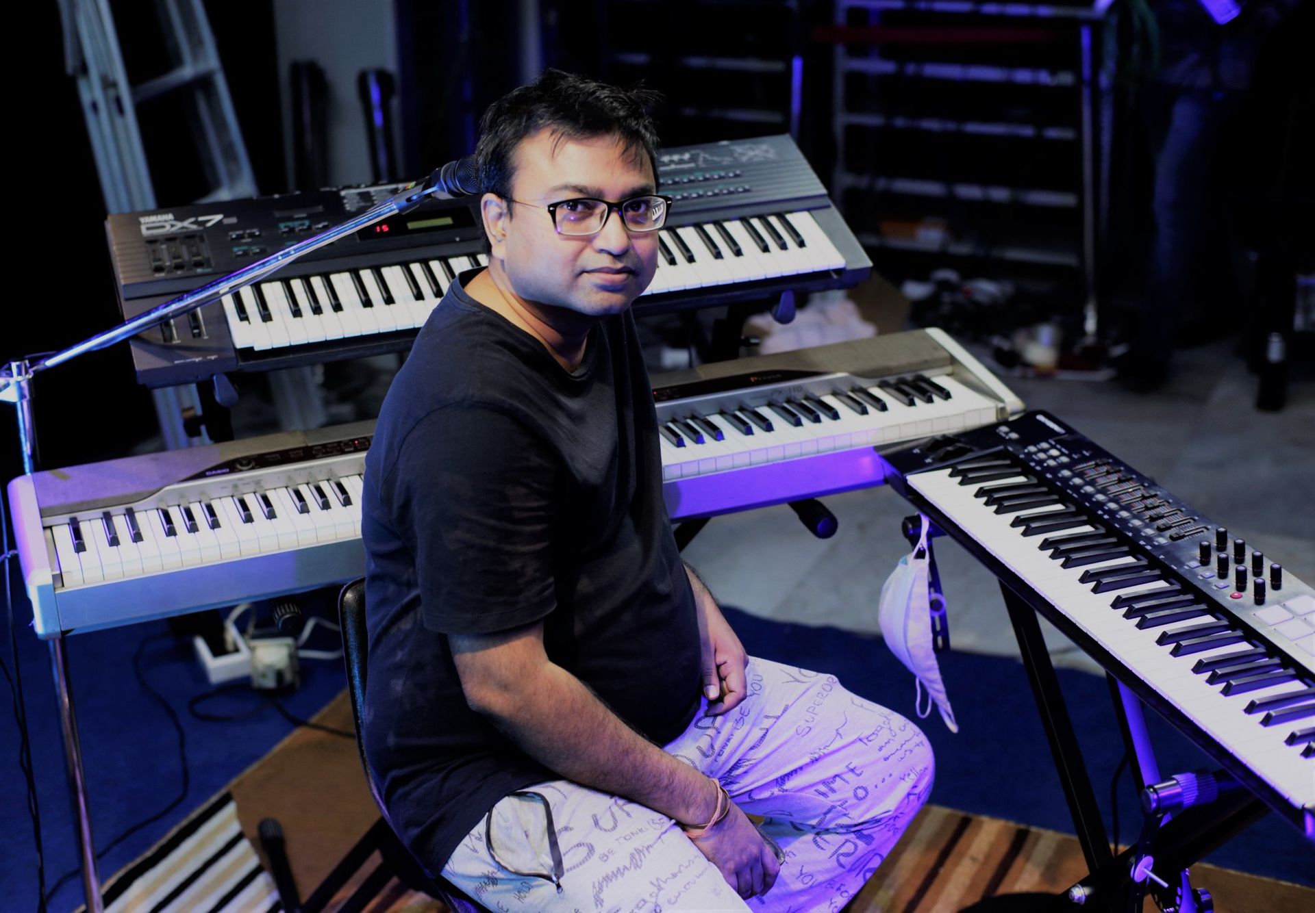 Drono Acharya sitting in front of a keyboard setup in a music studio, looking confident and focused.