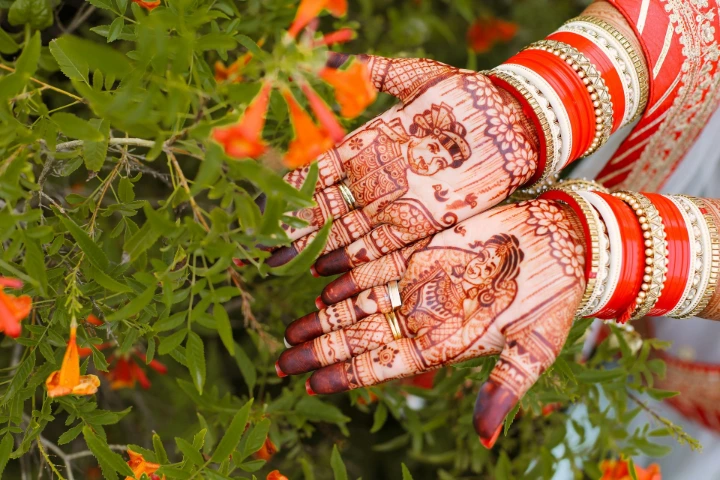 Bride's hands with custom mehndi showing groom and bride artwork